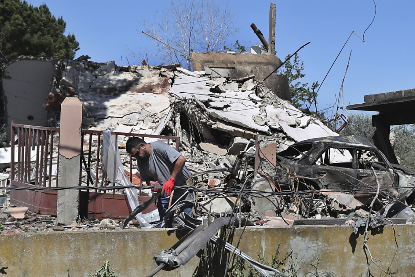 Un électricien libanais répare des câbles électriques devant une maison détruite par une frappe aérienne israélienne, à Alma al-Shaab, un village libanais frontalier avec Israël, dans le sud du Liban, Tsahal répondant à une attaque du Hezbollah. KEYSTONE