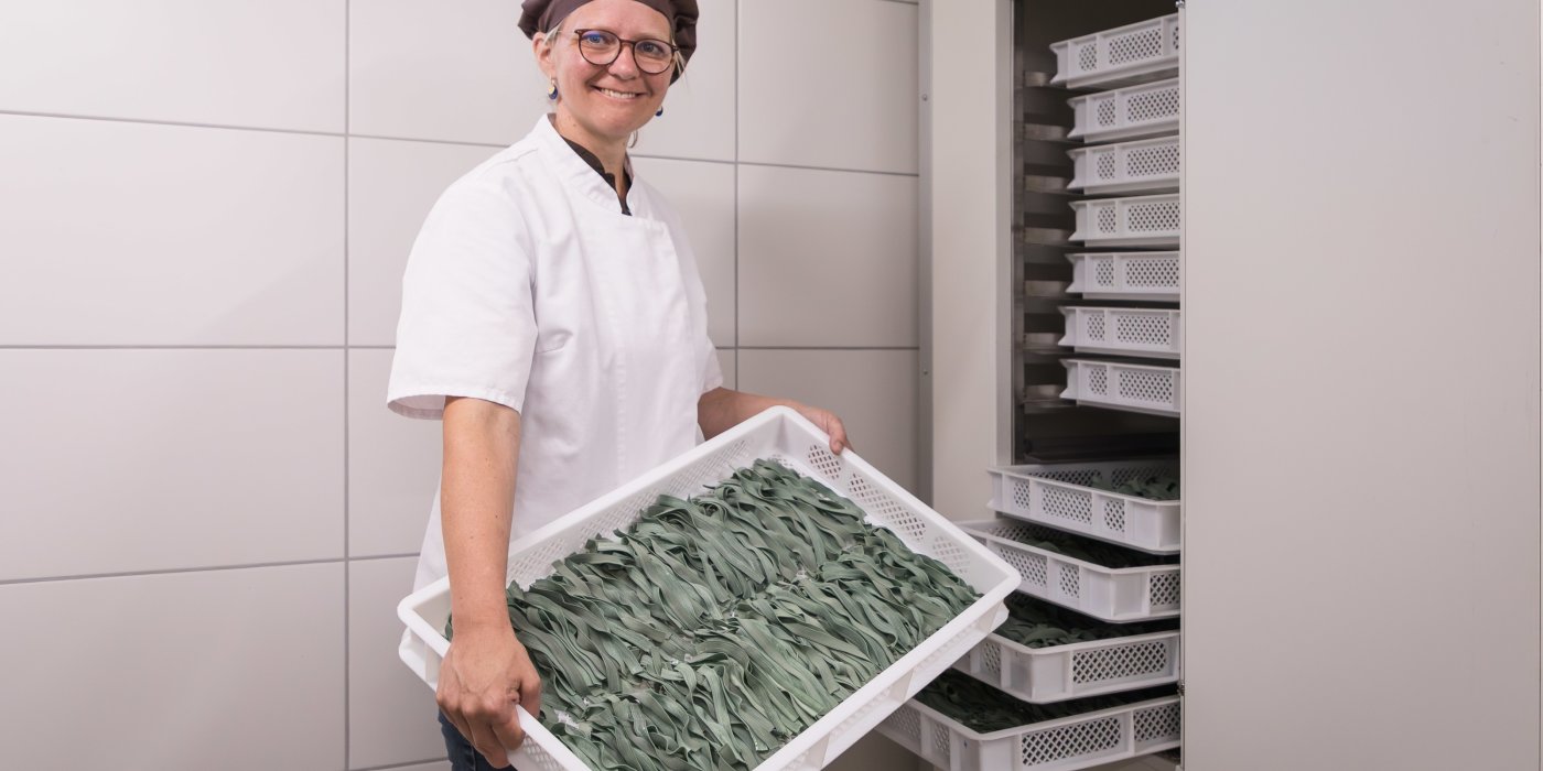 Miécourt, le 3 août 2026. Ferme des Tilleuls. Caroline Schori dans son laboratoire, tenant un bac de tagliatelles à la spiruline fraîchement fabriquées. Photo Claude-Alain Fauser.